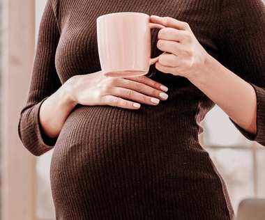 Elternzeitvertretung: Das Bild zeigt eine Schwangere, die eine Kaffeetasse auf ihrem Bauch abstellt.