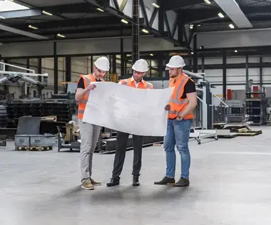 Interim Management Operations: Das Bild zeigt drei Männer in Arbeitskleidung in einer Produktionshalle. 