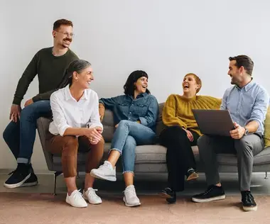 Interim Management Personalwesen: Das zeigt fünf Personen auf einer Couch, die sich miteinander unterhalten und lachen. 