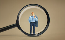 Das Bild zeigt eine Lupe, die einen Interim Manager vergrößert.