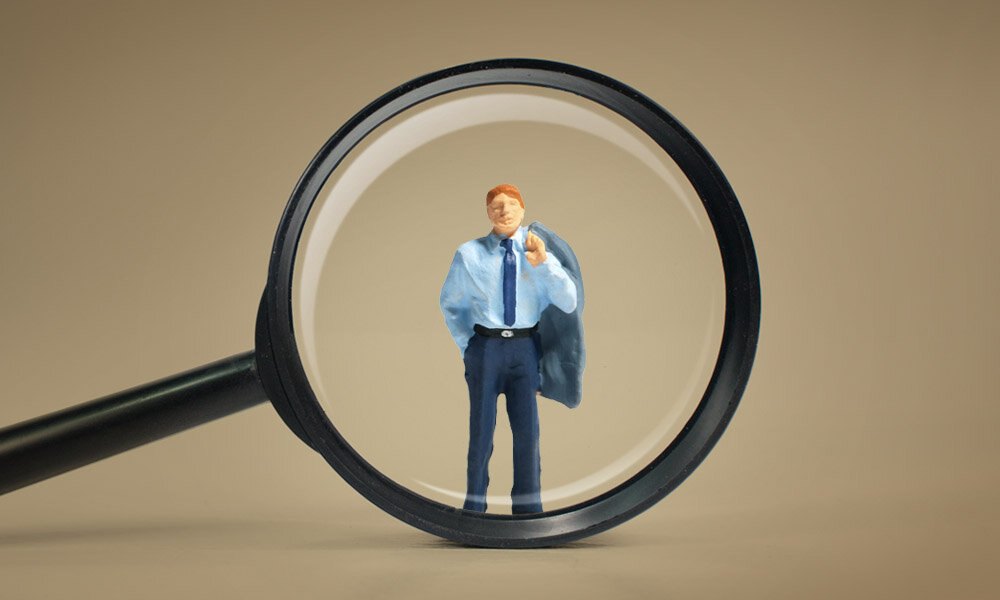 Das Bild zeigt eine Lupe, die einen Interim Manager vergrößert.