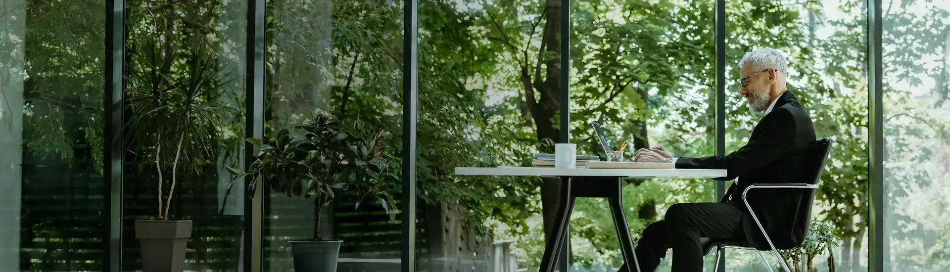 Interim Management CSR: Das Bild zeigt einen arbeitenden Manager, der vor einer Glasfront sitzt, hinter der die Natur zu sehen ist.