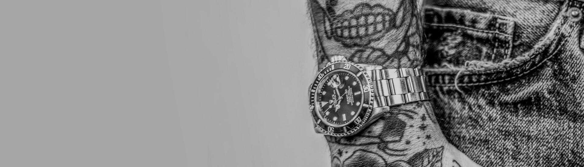 Das Bild zeigt den Arm eines tätowierten Mannes, der eine teure Uhr am Handgelenk trägt.