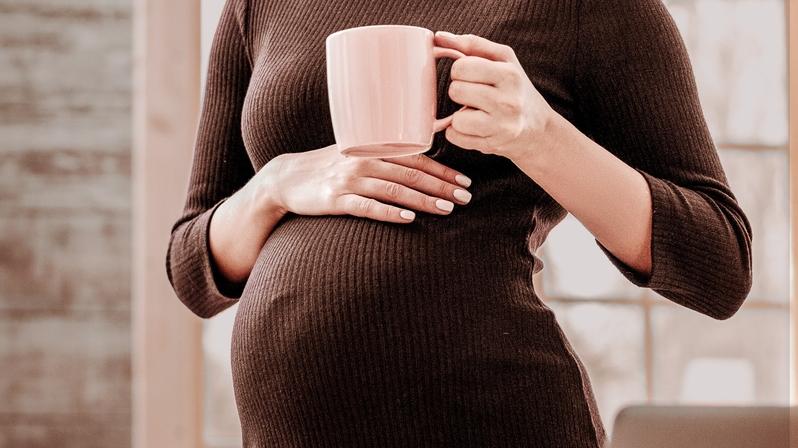 Elternzeitvertretung: Das Bild zeigt eine Schwangere, die eine Kaffeetasse auf ihrem Bauch abstellt.