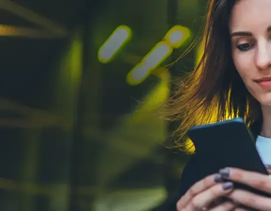Das Bild zeigt eine junge Frau, die auf ihr Smartphone schaut.