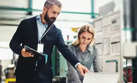 Interim Management Operations: Das Bild zeigt einen Operations-Manager, der seiner Kollegin etwas auf einem Laptop zeigt.